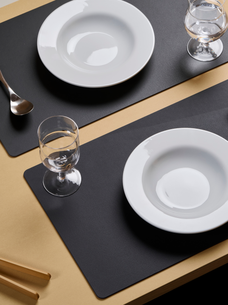 Aerial view of a linoleum dining table featuring a Faust medium-format PAD Mat in 4166 Charcoal, used as practical placemats for a meal setting