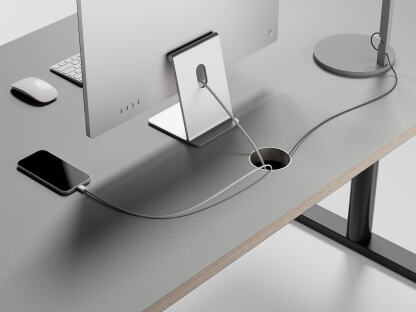 An ATS table by Faust featuring black metal round stands and a Pebble linoleum tabletop with plywood edges. It includes an aluminum cable management ring and is equipped with a computer, desk lamp, and an iPhone on charge.