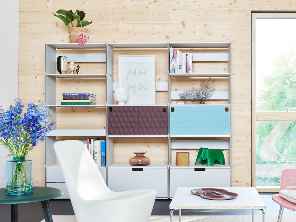 Plus Minus Regal von Faust aus Linoleum und MDF, eingerichtet mit Büchern und Objekten vor einer Wand aus hellem Holz.