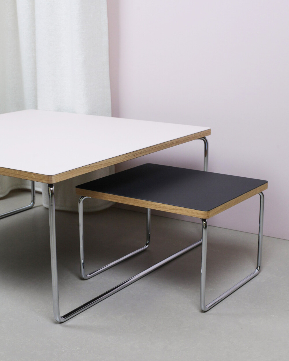 Low & Lower side tables by Faust made of linoleum in pink and black with chrome frame, in front of a light pink wall and curtain.