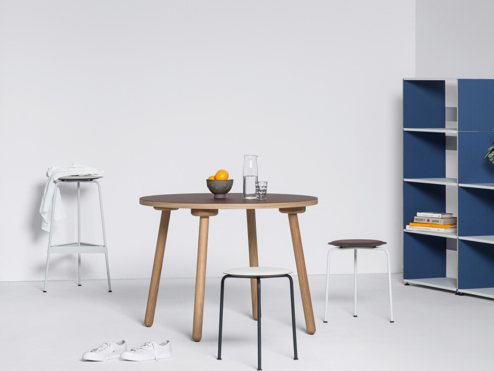 MT2 Tisch mit brauner Linoleumoberfläche und minimalistischen Holzbeinen, in einer hellen Interiorszene mit Tisch und Regal.