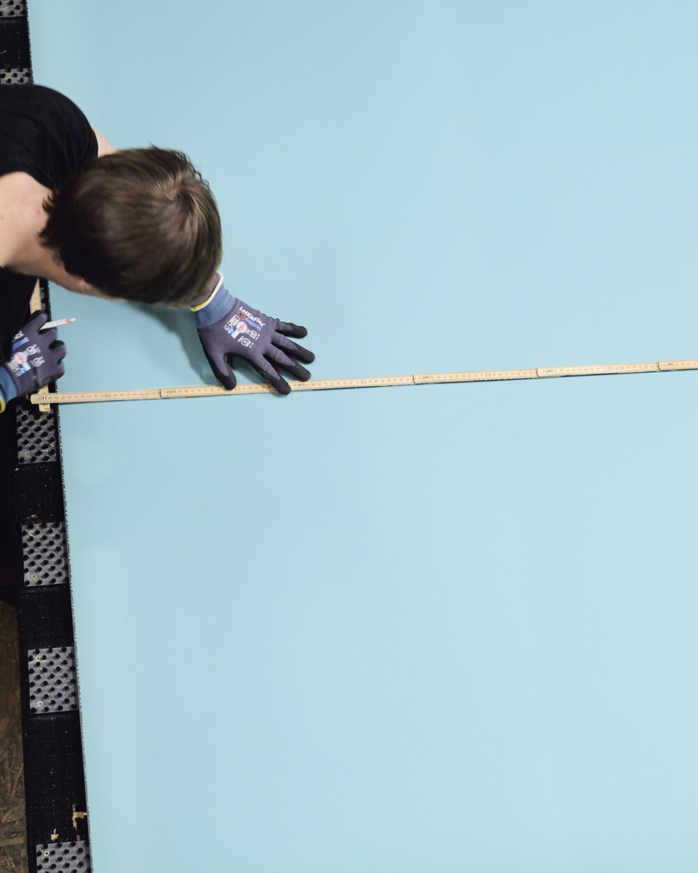 Tischplattenzuschnitt mit Linoleum in Hellblau – eine Hand fixiert einen Zollstock auf der Platte, Arbeitssituation bei der Maßaufnahme.