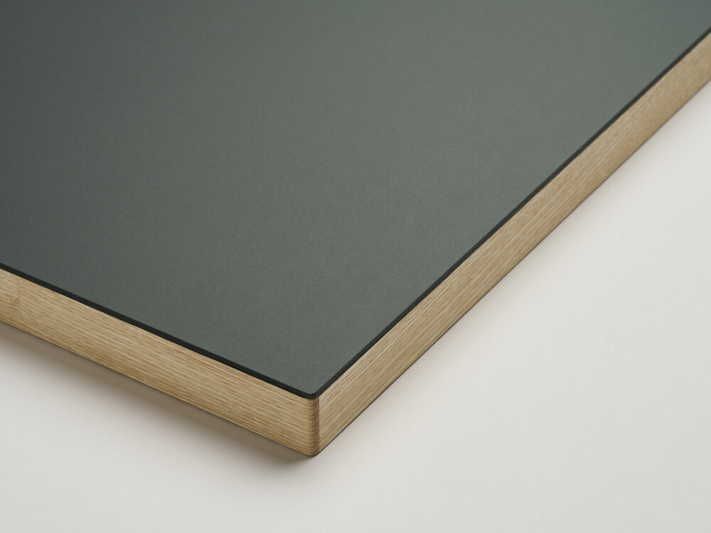 Fist table top with matt linoleum surface in pewter (dark gray-green) and oiled, rounded solid wood edge made of ash.