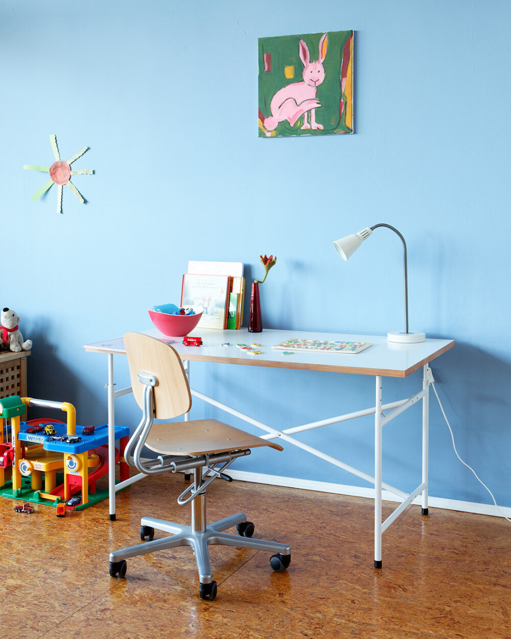 E2 children's desk with white top in the children's room, used as a workspace with lamp, books, and toys.