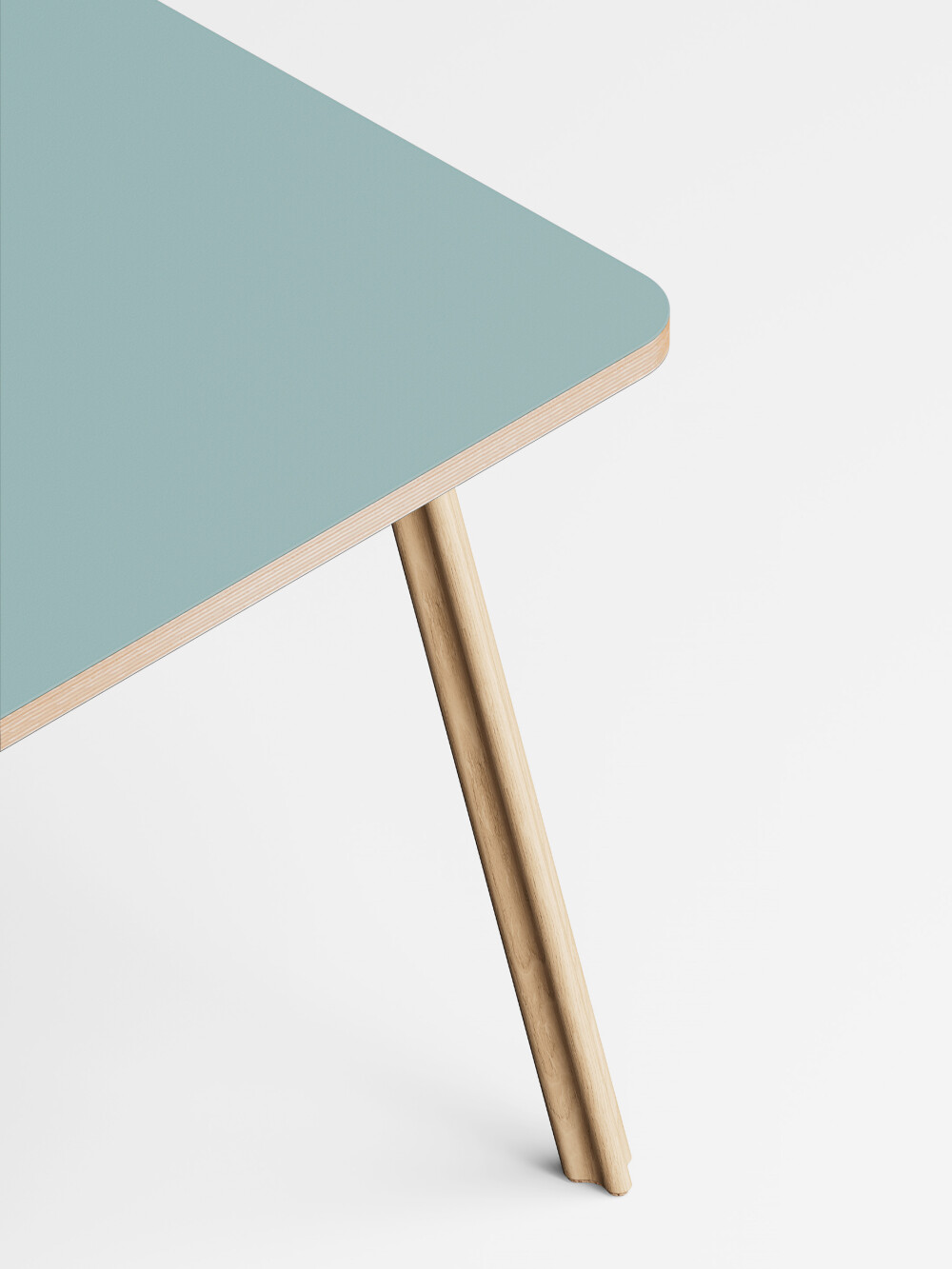 Detailaufnahme des Beam Tischbeins aus massivem Eichenholz mit Korkfüßen an einer hellblauen Linoleum Tischplatte.