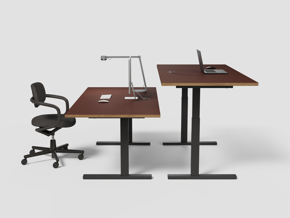 Two height-adjustable ATS desks with burgundy linoleum tops and black frames, one in sitting mode, the other in standing mode.