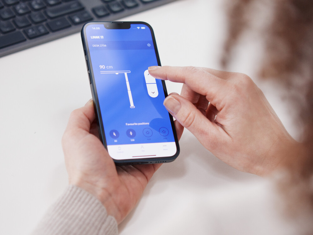 Person steuert die Höhe eines ATS Schreibtischs von Michel Charlot über die LINAK App am Smartphone.