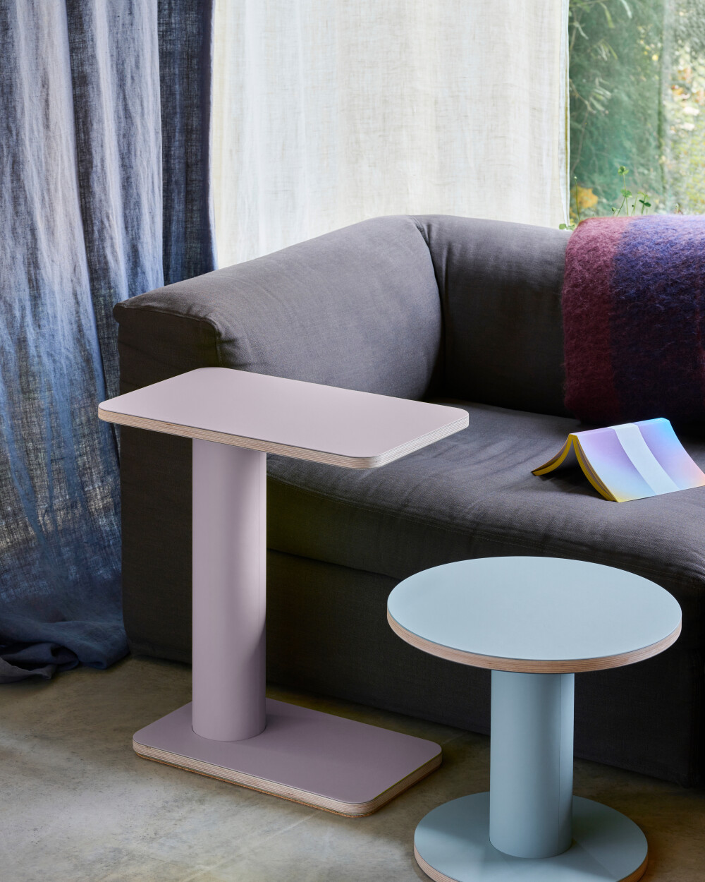 OFF-CUT side tables by Faust with linoleum surfaces in dusky pink and light blue, next to a gray sofa in a cozy setting.