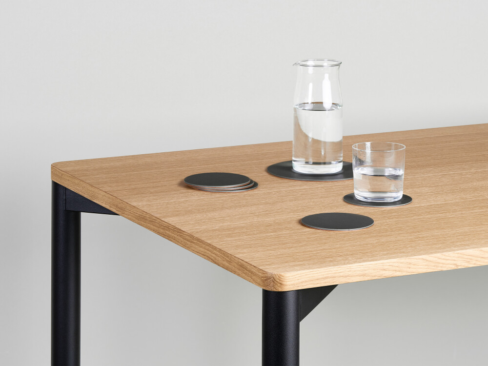 Outline table by Faust with light oak veneer tabletop and black frame, decorated with water glasses and a carafe.