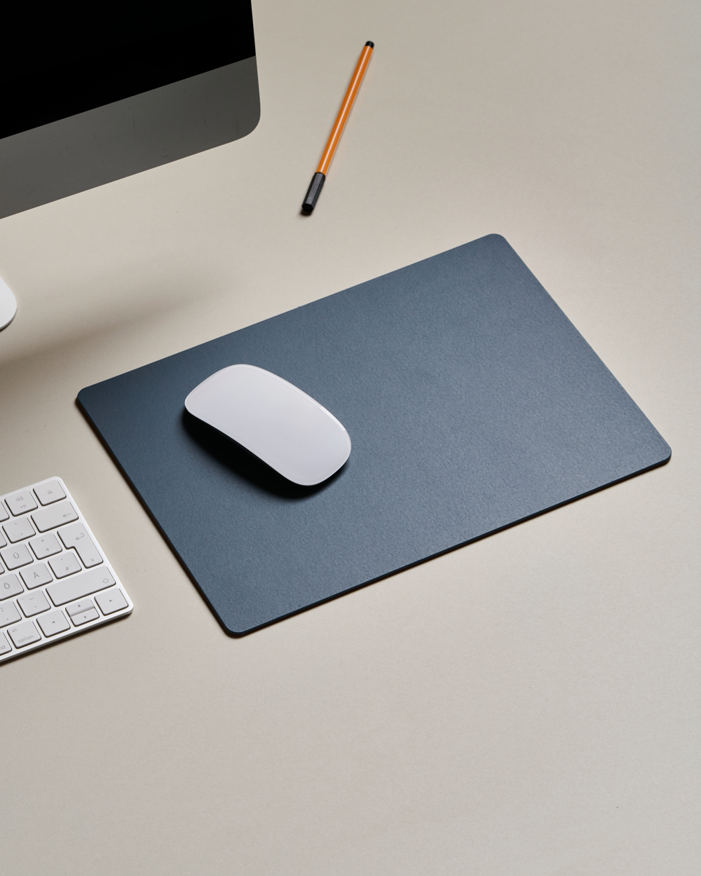 PAD linoleum desk pad in smokey blue on a light-coloured desk with keyboard, mouse and pen.